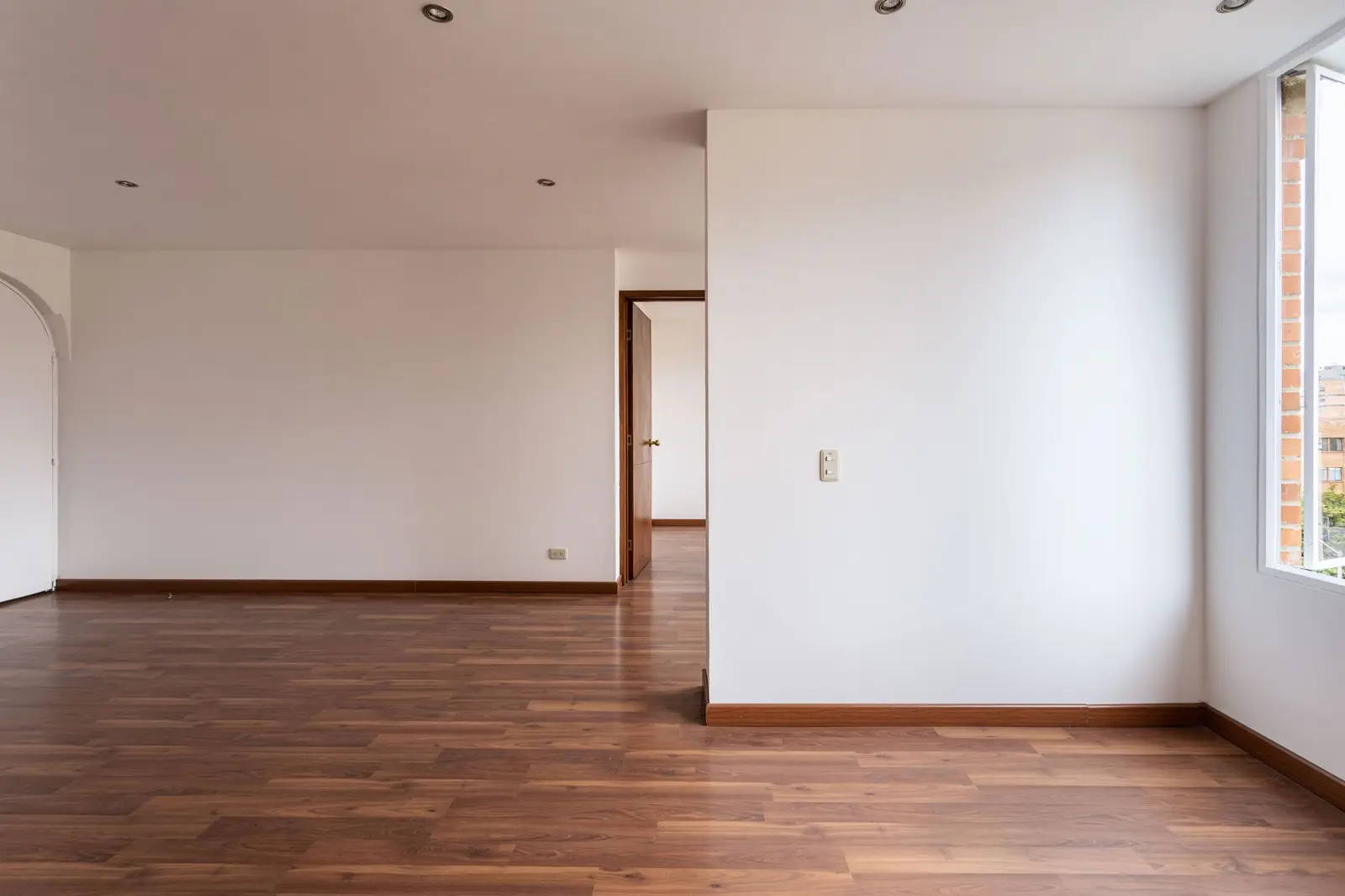Leeres Zimmer mit weißen Wänden und Holzboden, bereit für die Übergabe